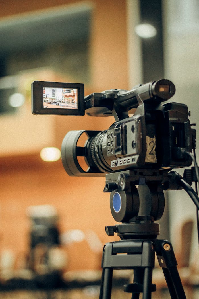 Close-up of a video camera on tripod capturing an indoor scene.